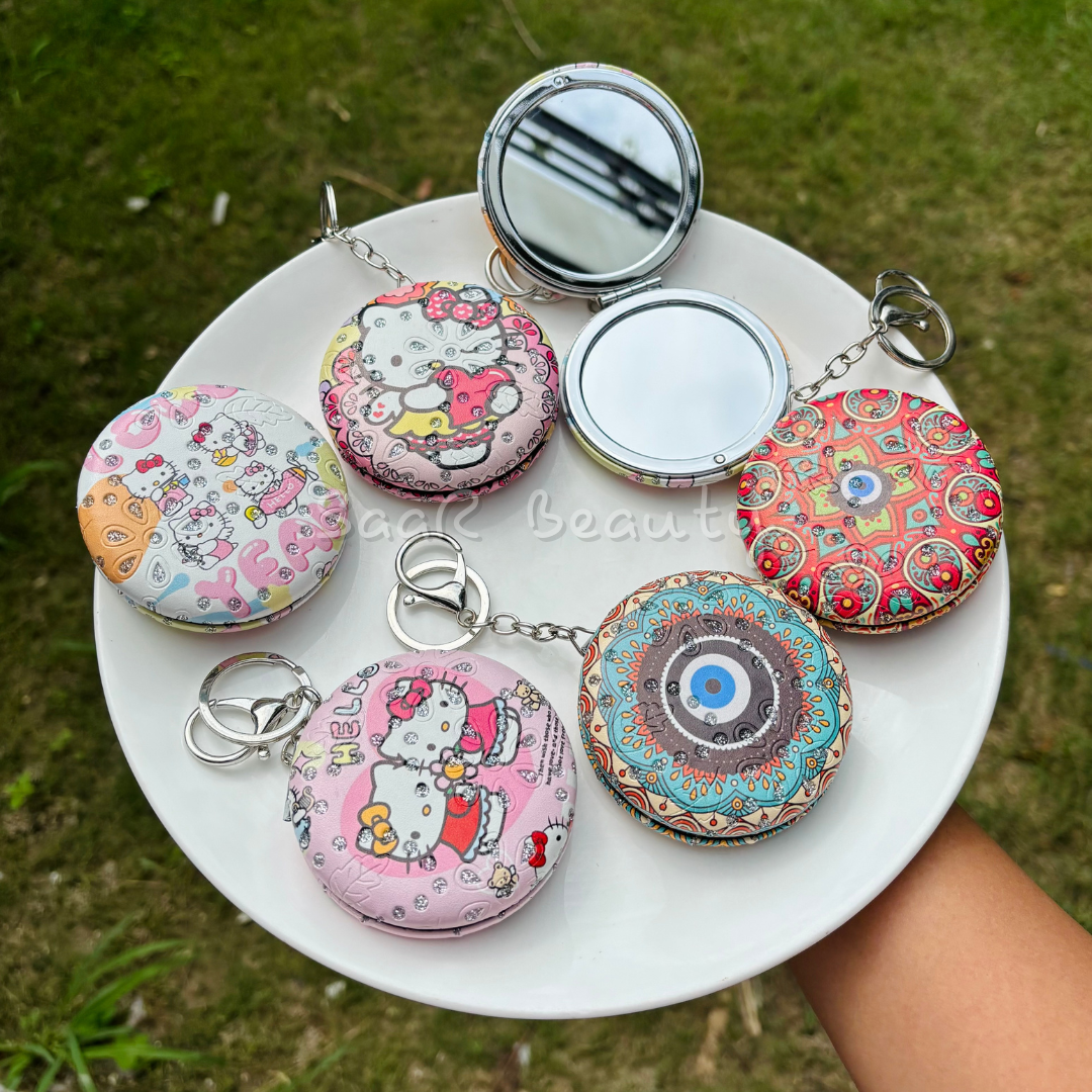 Colorful compact mirrors with keychains on a white plate outdoors. Premium Saar Beauty keychain mirrors with Hello Kitty and Evil Eye designs – compact, portable, and durable pocket mirrors for women and girls