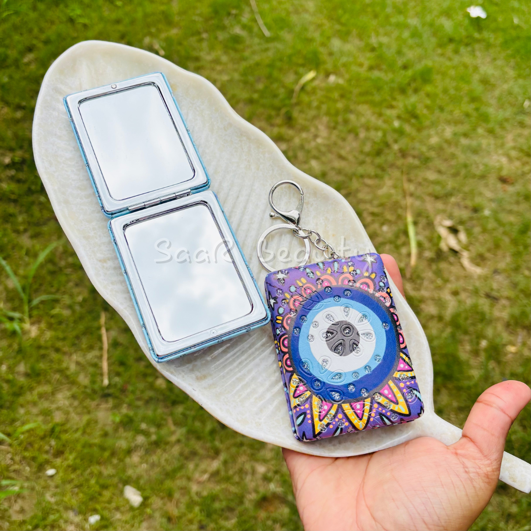 Person holding a colorful MP3 player case with a silver square object on a leaf against a grassy background Cute Kitty and Evil Eye Keychain Pocket Mirrors – Portable & Stylish Design by Saar Beauty
