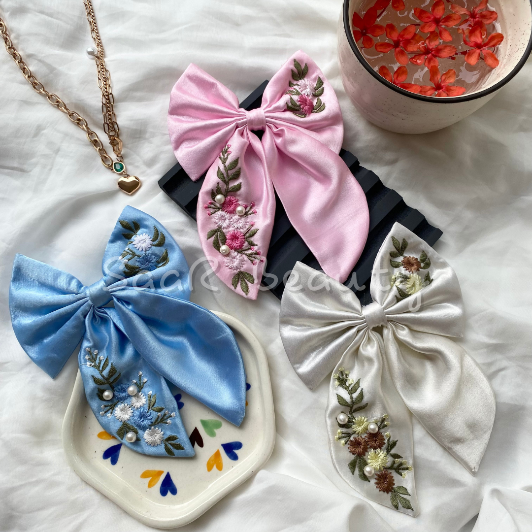 Elegant Satin Bow Hair Clip with hand-embroidered floral design, available in pink, blue, and white. Perfect for thick, thin, and long hair β a must-have hair accessory for women and girls by Saar Beauty