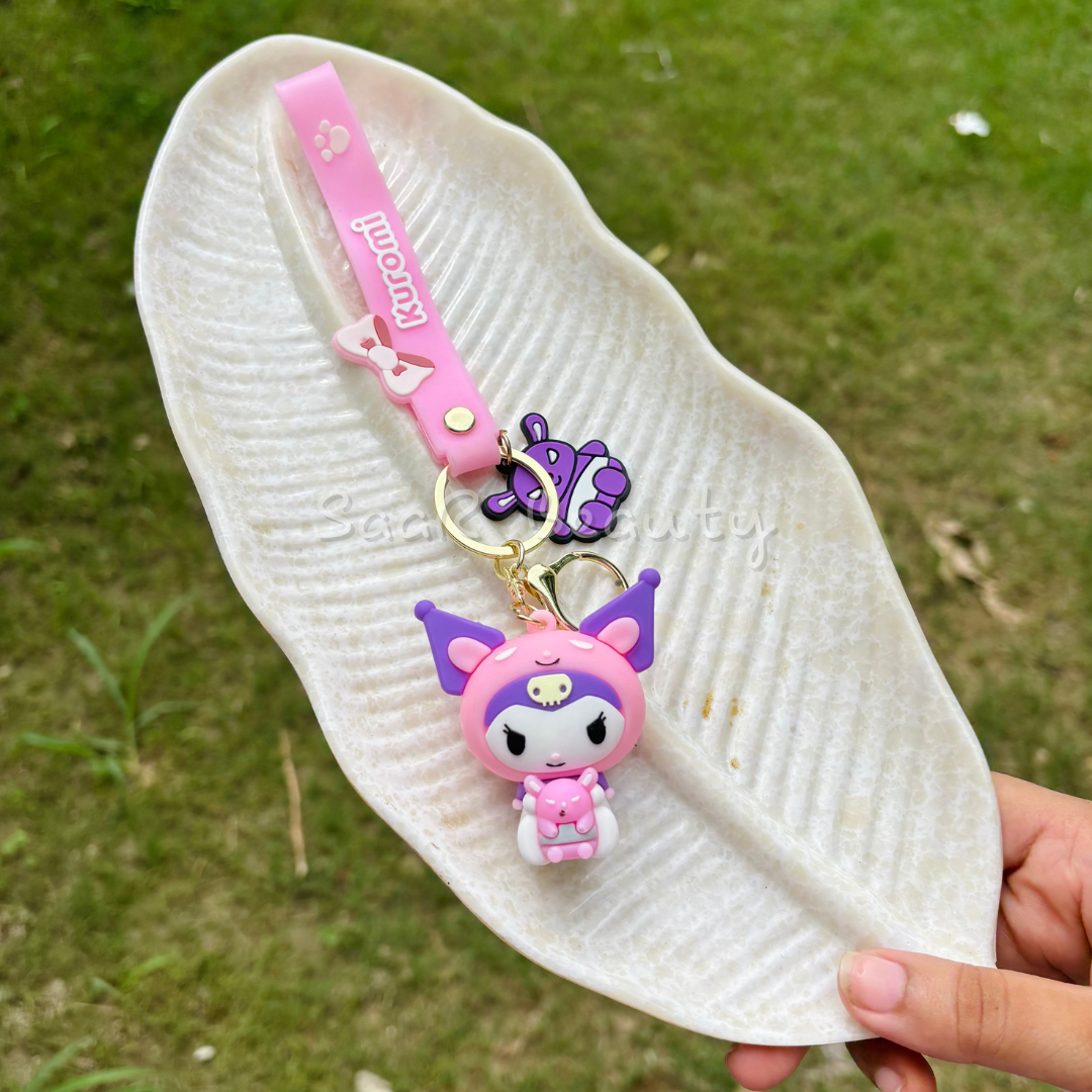 White sandal with a pink and purple keychain featuring a cartoon character on a grassy background. Premium cute cartoon keychains by Saar Beauty featuring Hello Kitty, Shinchan, Kuromi, Starbucks drink, boba tea, and pink bow designs – durable, trendy, and stylish for women, kids, and girl