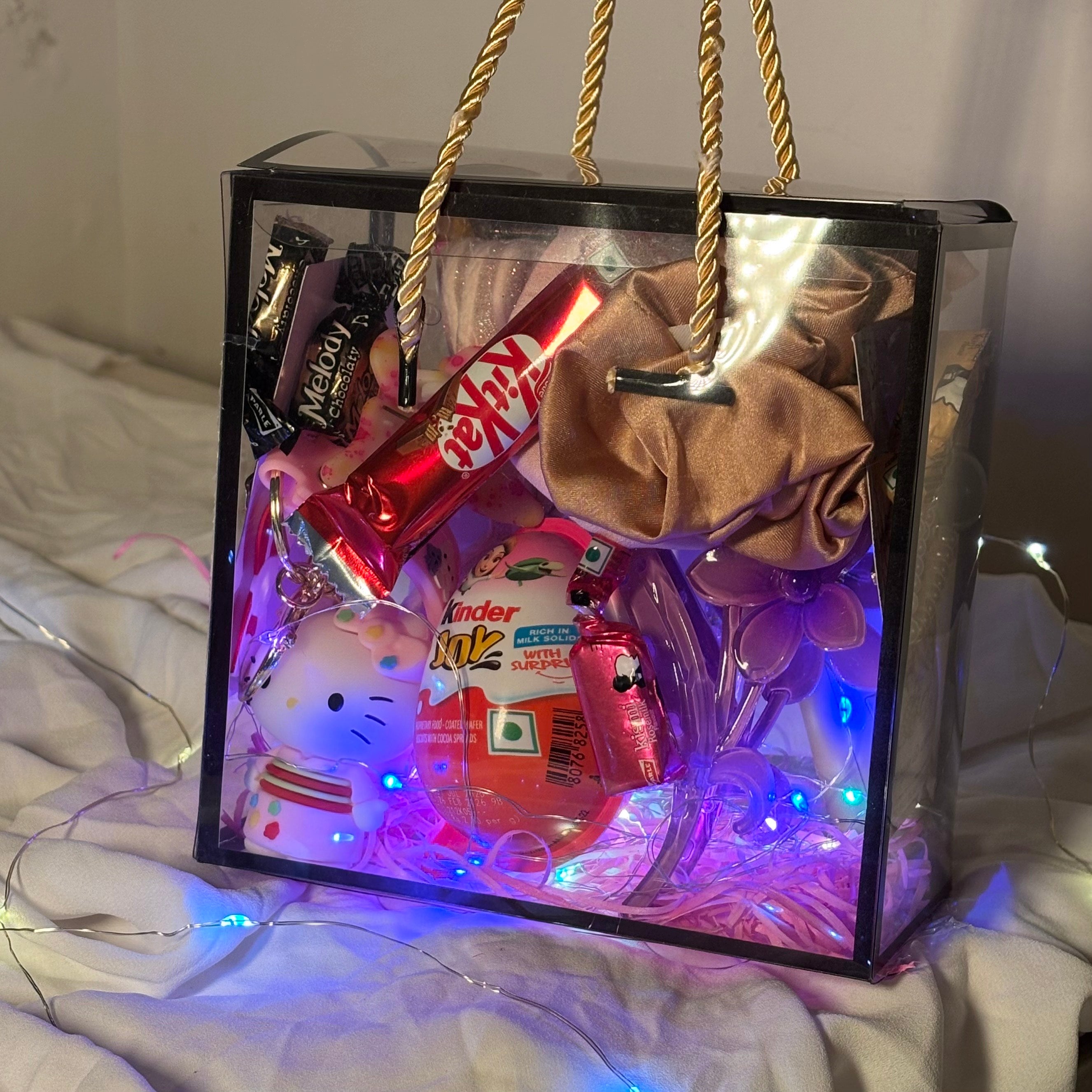 Decorative gift box with LED lights containing small items on a white surface. Gift hamper for women with earrings, scrunchies, clutchers and Kinder Joy