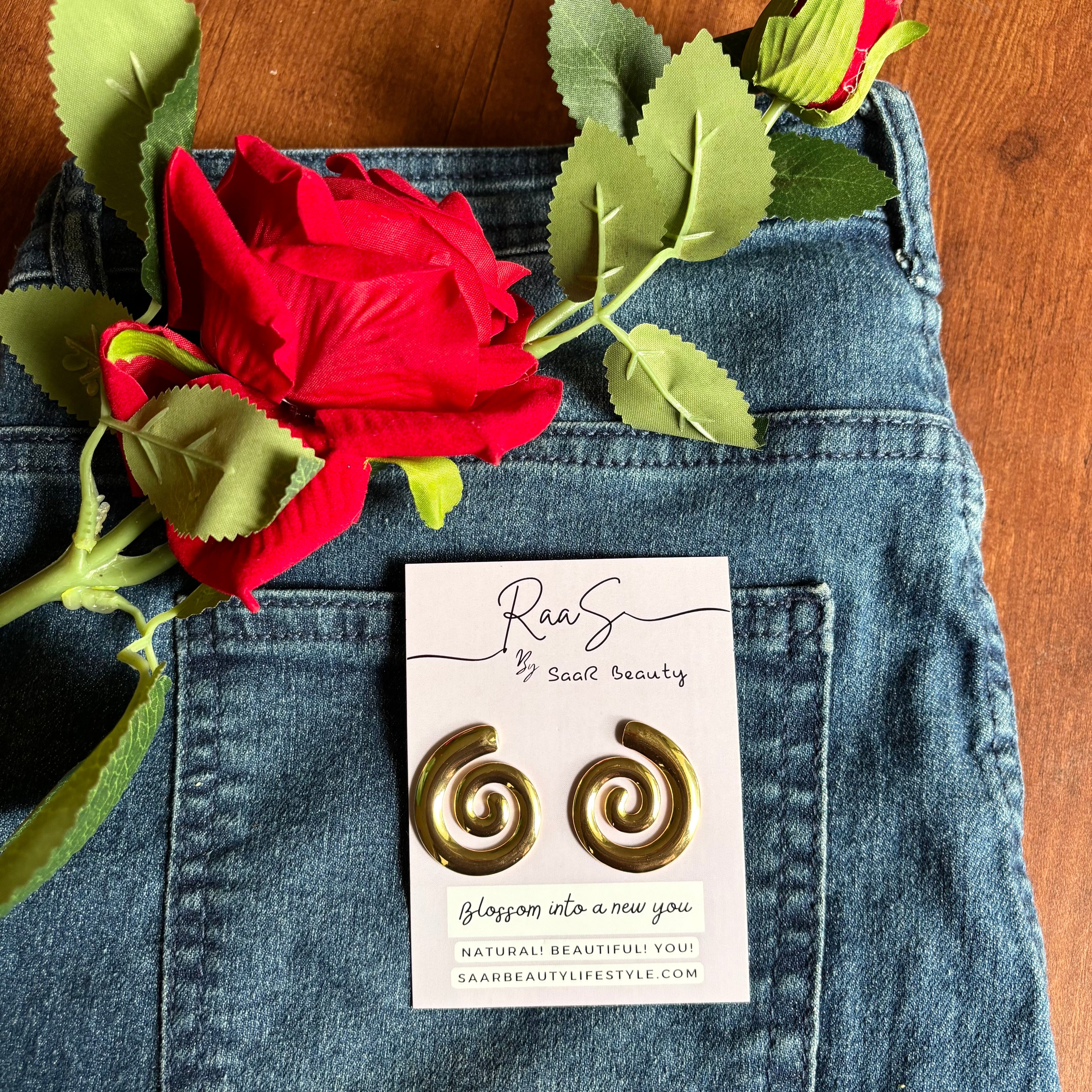Gold spiral earrings on a card with a red rose and green leaves on blue denim fabric.