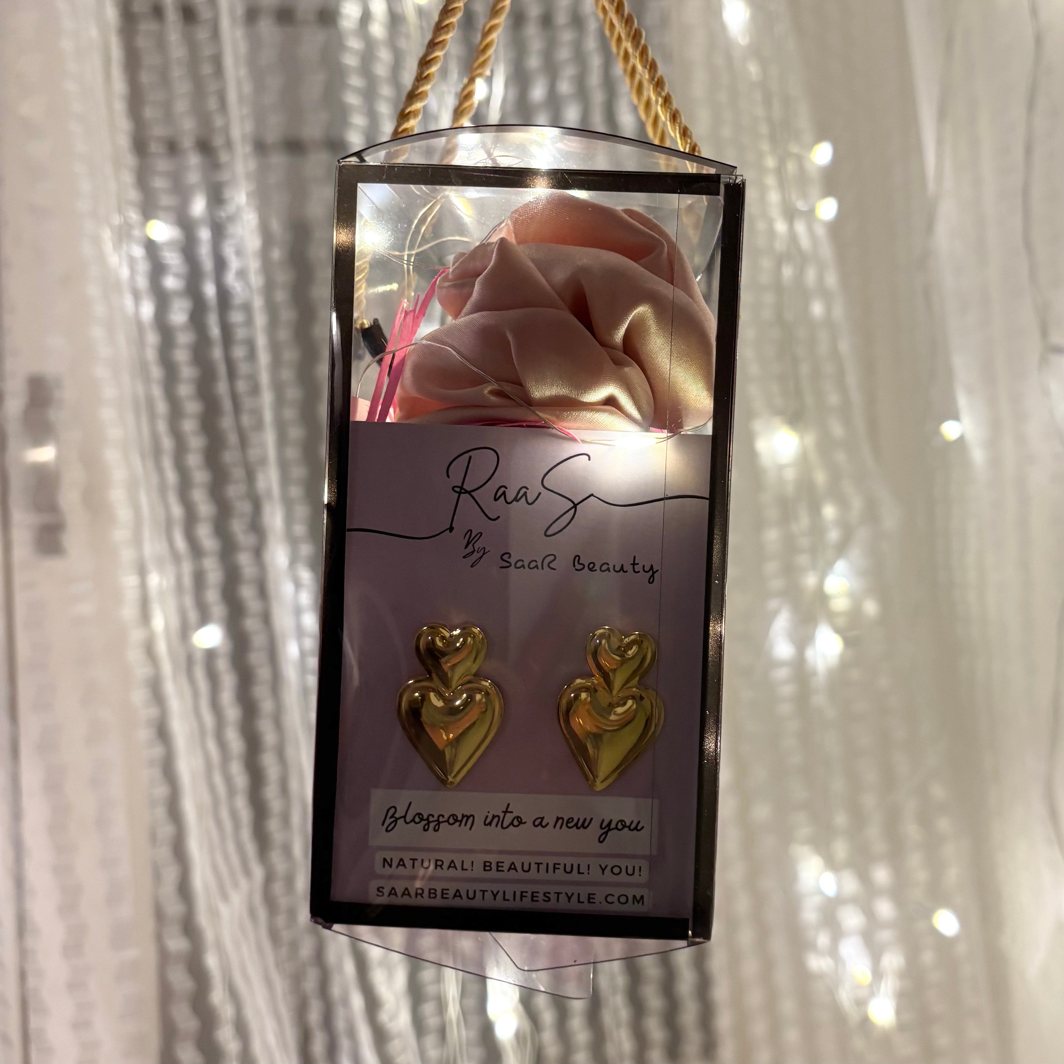 Gold heart-shaped earrings in a clear packaging with a branded card against a textured white background.