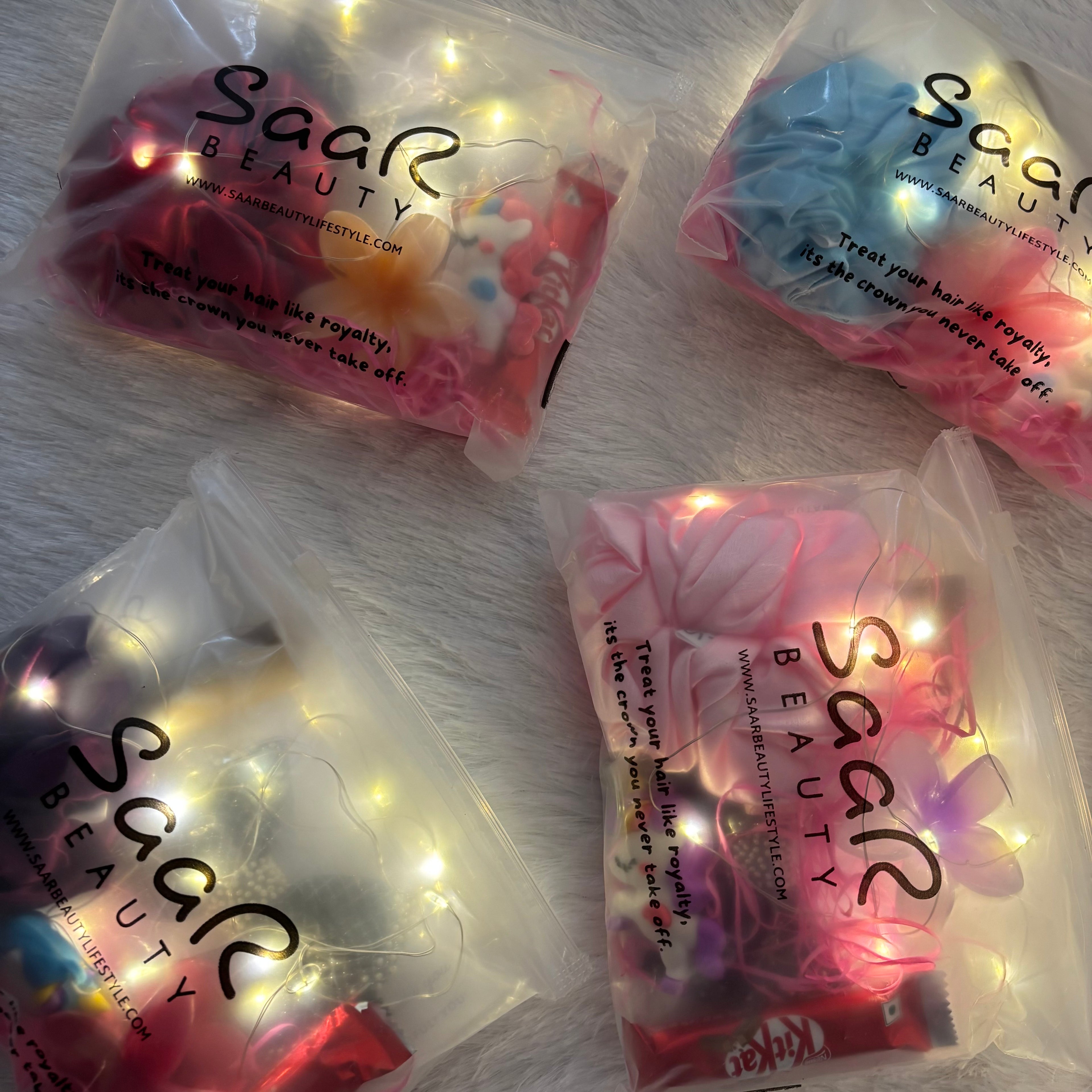 Four packages of Saar Beauty hair accessories on a white surface with string lights.Pinterest aesthetic fairy light gift hamper Saar Beauty