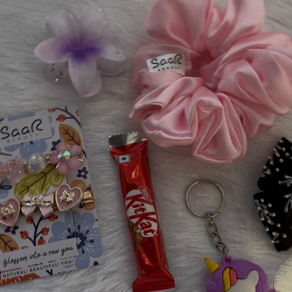 Pink scrunchies, hair clips, KitKat bar, and keychain on a textured surface