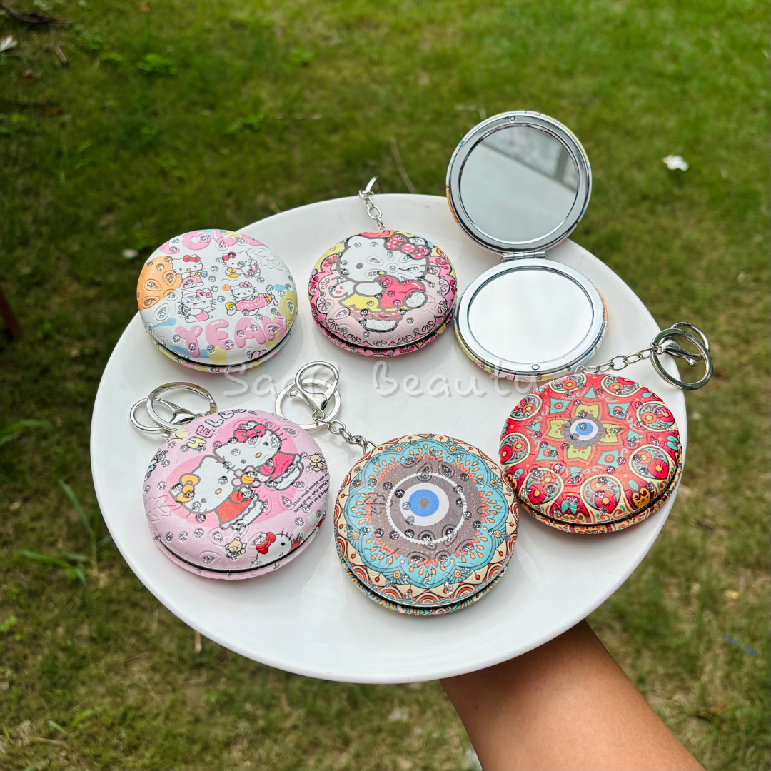 Colorful compact mirrors with keychains on a white plate outdoors.Premium Saar Beauty keychain mirrors with Hello Kitty and Evil Eye designs – compact, portable, and durable pocket mirrors for women and girls