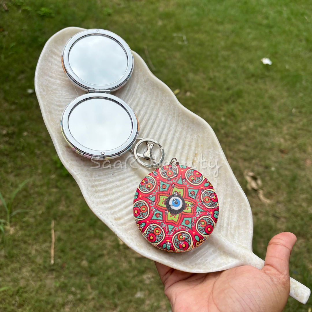 Colorful keychain with a pattern held over a white sandal on grass Premium Saar Beauty keychain mirrors with Hello Kitty and Evil Eye designs – compact, portable, and durable pocket mirrors for women and girls