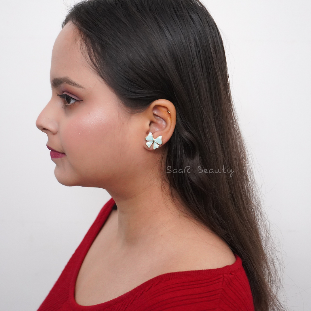 Saar Beauty’s artistic blue and gold earrings styled on a rustic stone backdrop.