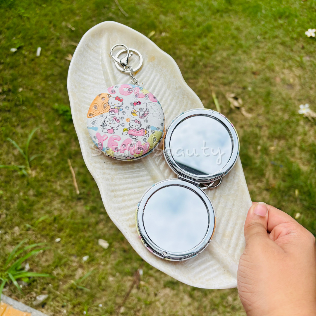 Two compact mirrors on a white leaf with grass in the background Premium Saar Beauty keychain mirrors with Hello Kitty and Evil Eye designs – compact, portable, and durable pocket mirrors for women and girls