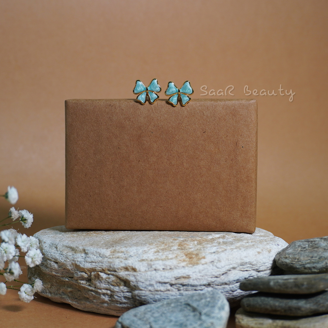 Saar Beauty’s artistic blue and gold earrings styled on a rustic stone backdrop.