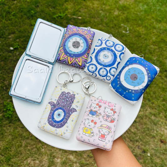 Collection of colorful keychains and pouches on a white plate with grass background Cute Kitty and Evil Eye Keychain Pocket Mirrors – Portable & Stylish Design by Saar Beauty