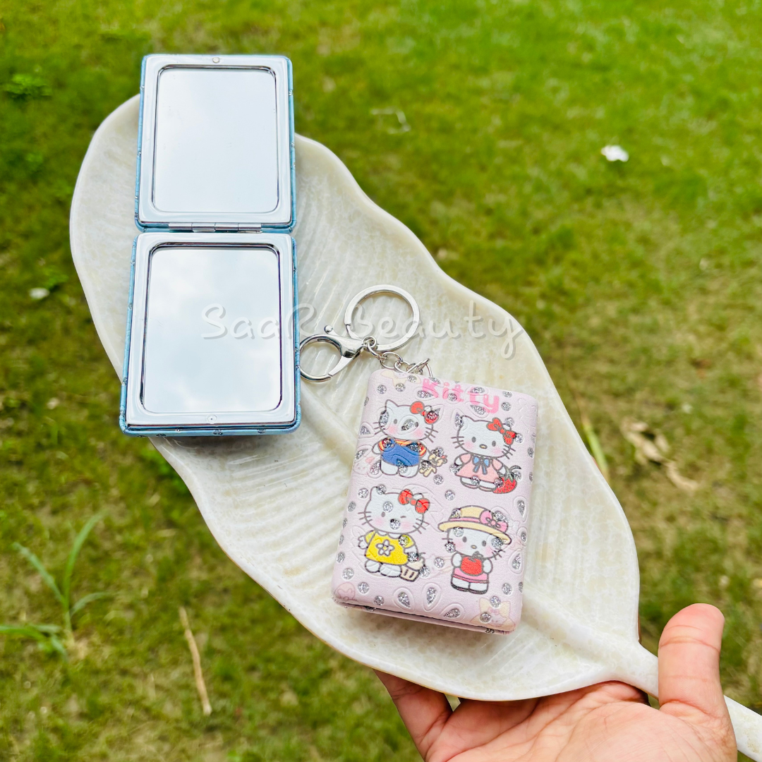 Compact mirror and keychain with cartoon design held over grass Cute Kitty and Evil Eye Keychain Pocket Mirrors – Portable &amp; Stylish Design by Saar Beauty