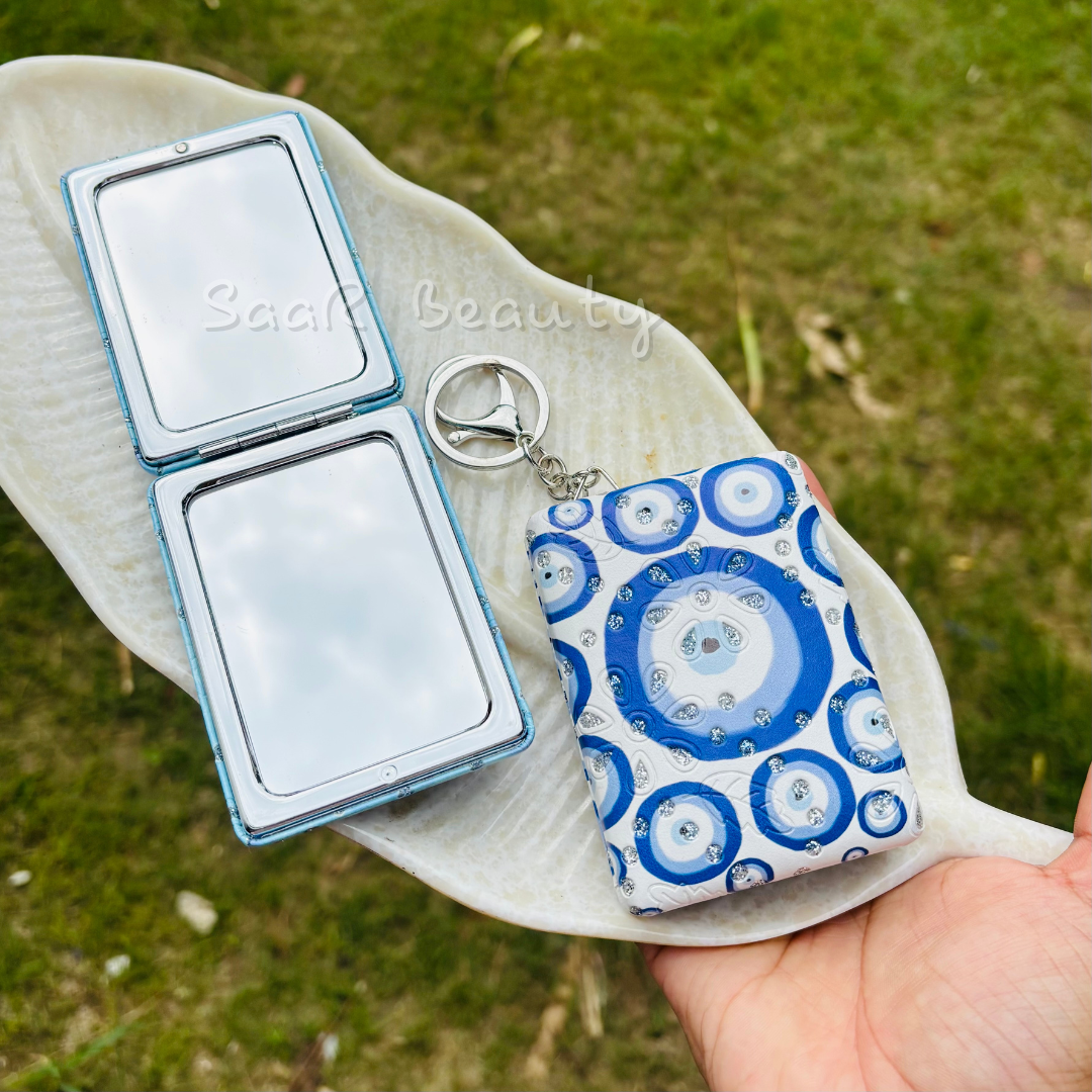 Compact mirror and patterned pouch on a leaf with 'Sara Beauty' branding. Cute Kitty and Evil Eye Keychain Pocket Mirrors – Portable & Stylish Design by Saar Beauty