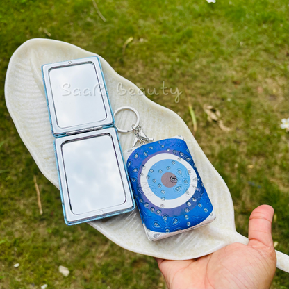 Compact mirror and blue evil eye keychain on a white cloth with grass  Cute Kitty and Evil Eye Keychain Pocket Mirrors – Portable & Stylish Design by Saar Beautybackground