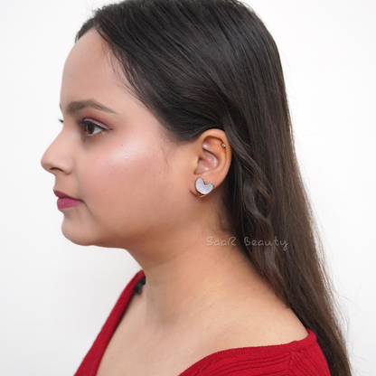 Close-up of lightweight heart earrings in white enamel with gold accents, styled on a neutral backdrop.