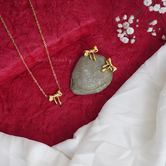 Minimalist gold-plated small bow necklace and earrings set displayed on red and white fabric.