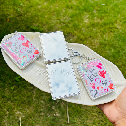 Compact mirror with decorative case held over a green grass background