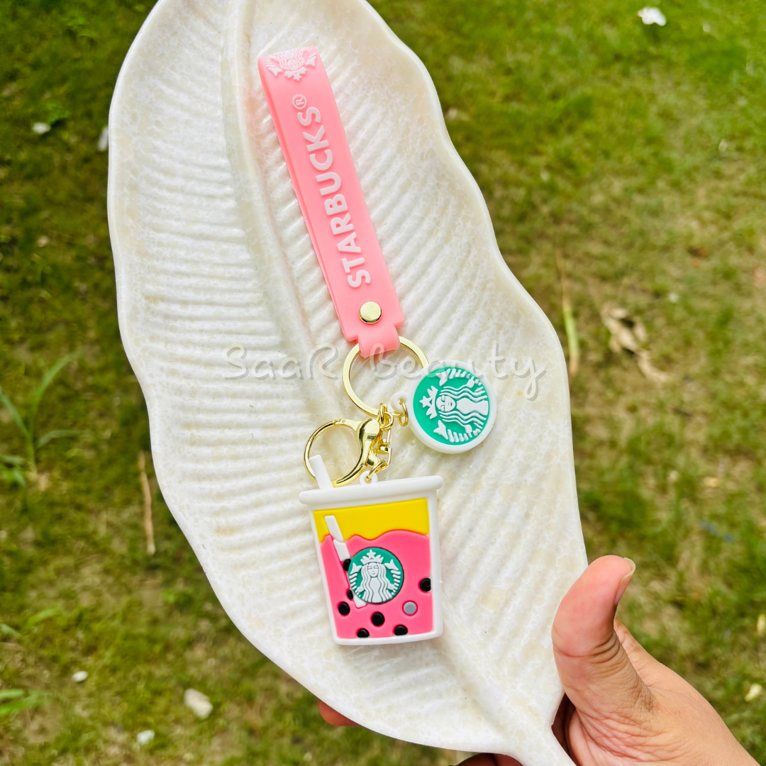 White sandal with a pink Starbucks keychain on a grassy background Premium cute cartoon keychains by Saar Beauty featuring Hello Kitty, Shinchan, Kuromi, Starbucks drink, boba tea, and pink bow designs – durable, trendy, and stylish for women, kids, and girl