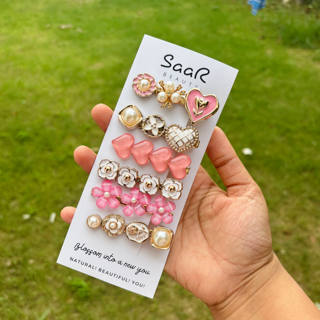Premium Korean hair clip set by Saar Beauty with pearl, heart, and floral designs – trendy and stylish hair accessories for women, kids, and girls. Hand holding a package of pink and gold earrings with &