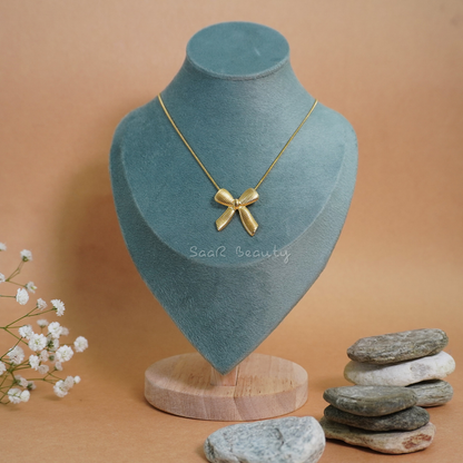 A gold chain necklace with a bow-shaped pendant displayed on a teal velvet bust.