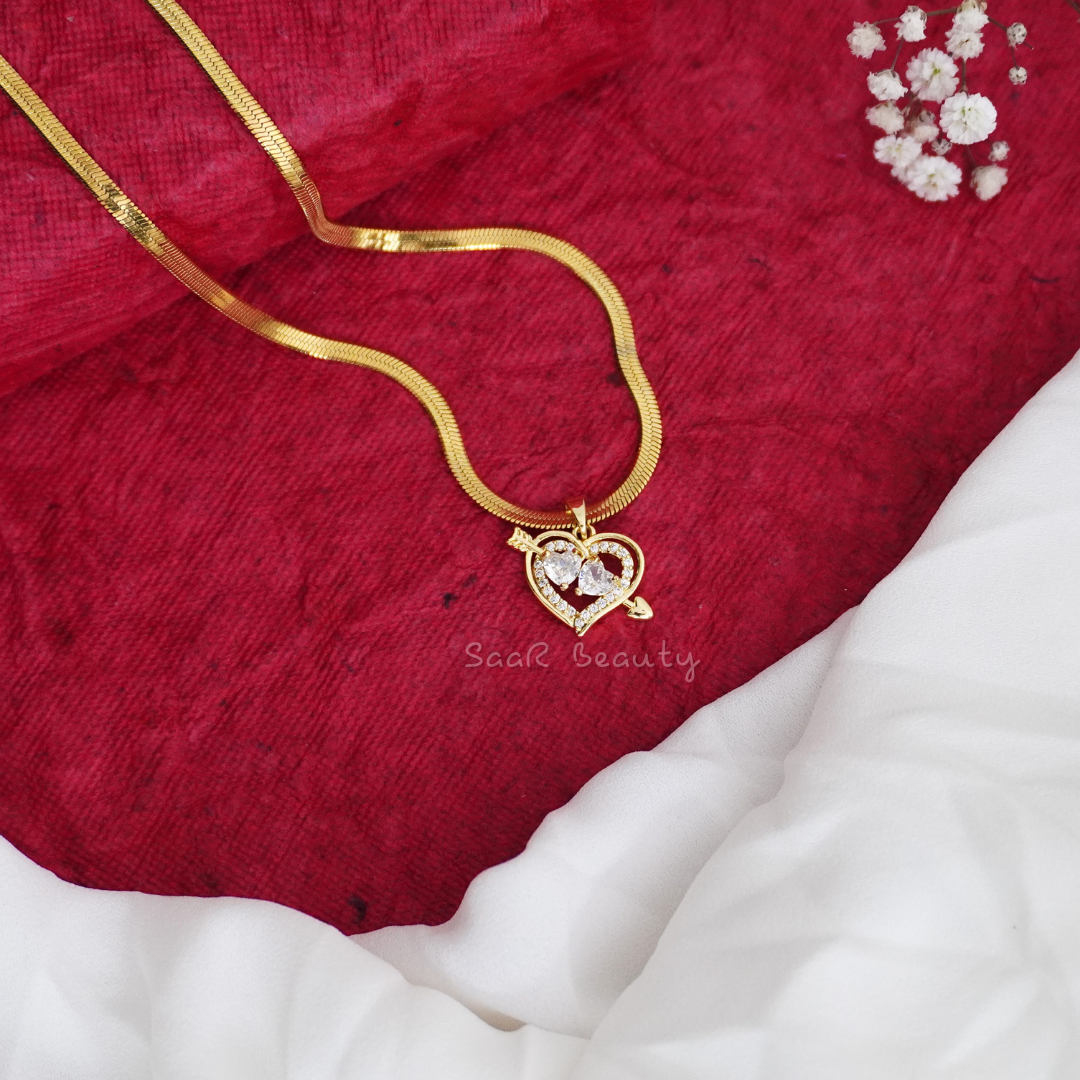 A gold snake chain necklace with a glossy white heart pendant.