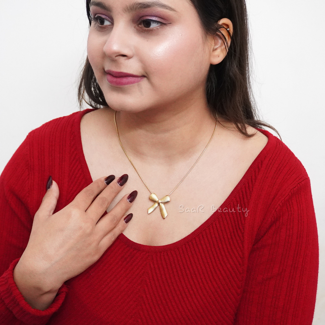 A model wearing a gold chain necklace with a bow-shaped pendant, styled with a minimalist outfit for an elegant look.