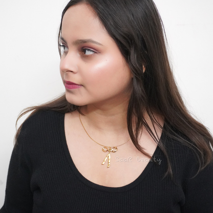 Model wearing a gold-tone bow-shaped stainless steel pendant necklace, highlighting its delicate and elegant design with a stylish outfit in natural light.