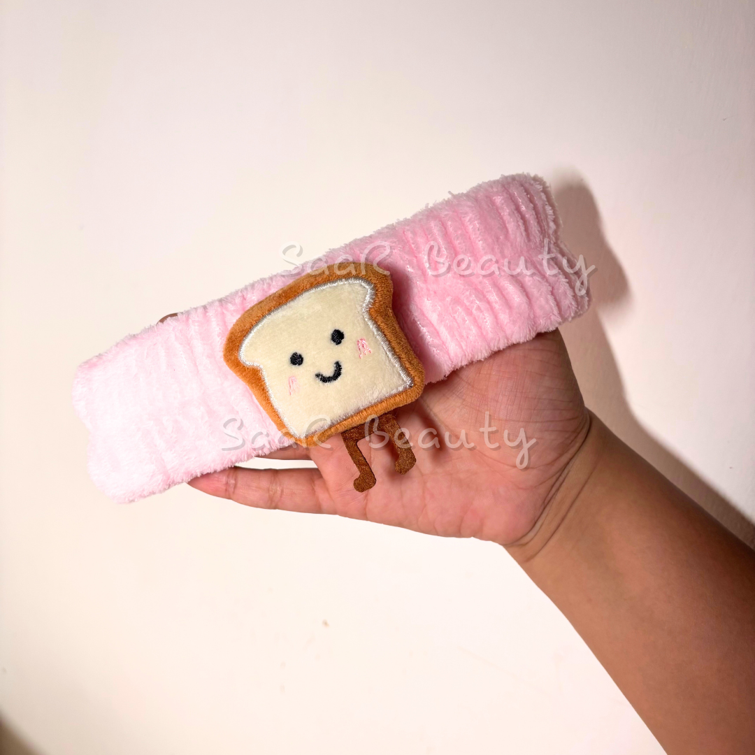 Hand holding a pink towel with a cute bread character on a light background Pink plush skincare headband with bread design and water-absorbing hand wraps