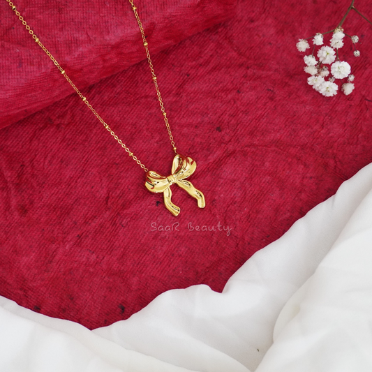 SaaR Beauty's golden bow pendant necklace, paired with a red sweater, showcasing minimalist charm.