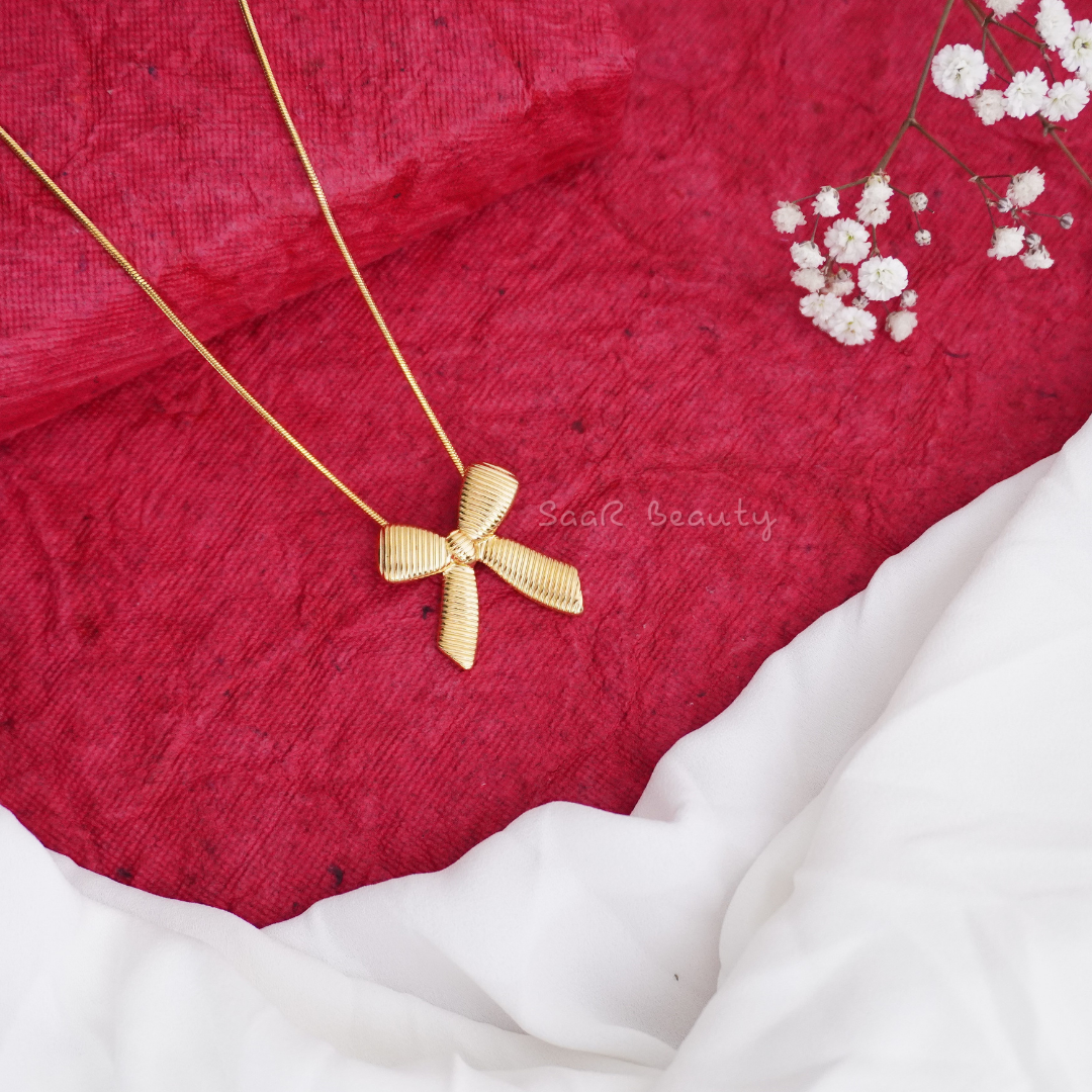 A gold chain necklace with a bow-shaped pendant displayed 