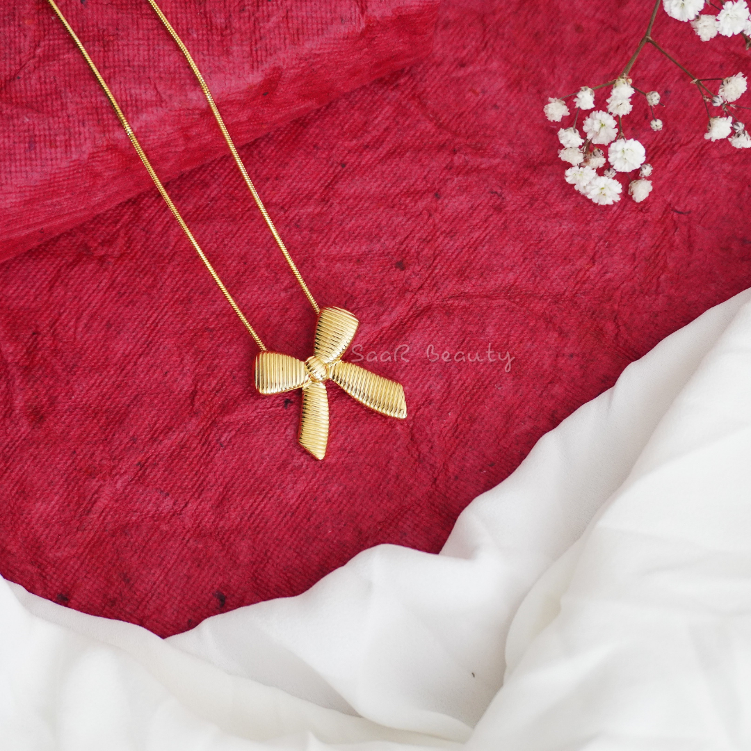 A gold chain necklace with a bow-shaped pendant displayed 