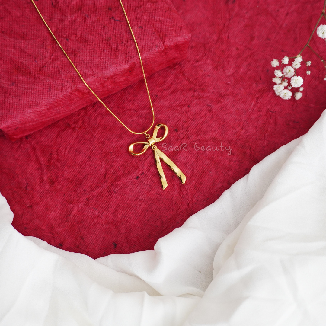 A gold-tone bow-shaped stainless steel pendant necklace, highlighting its delicate and elegant design with a stylish outfit in natural light.