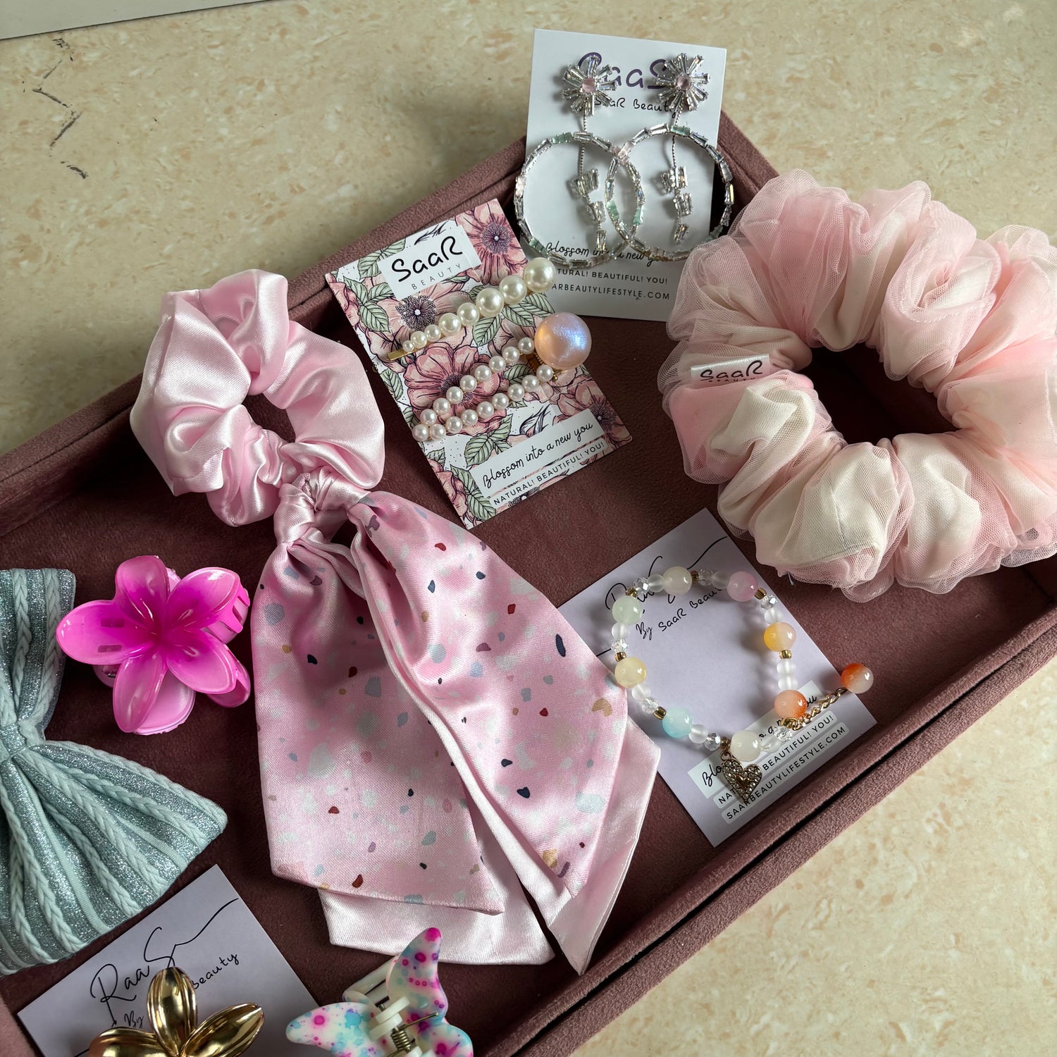 Premium Rakshabandhan gift box with shimmer bow, satin scarf scrunchie, flower hair claw, butterfly clip, jewelry, and hair accessories by Saar Beauty.