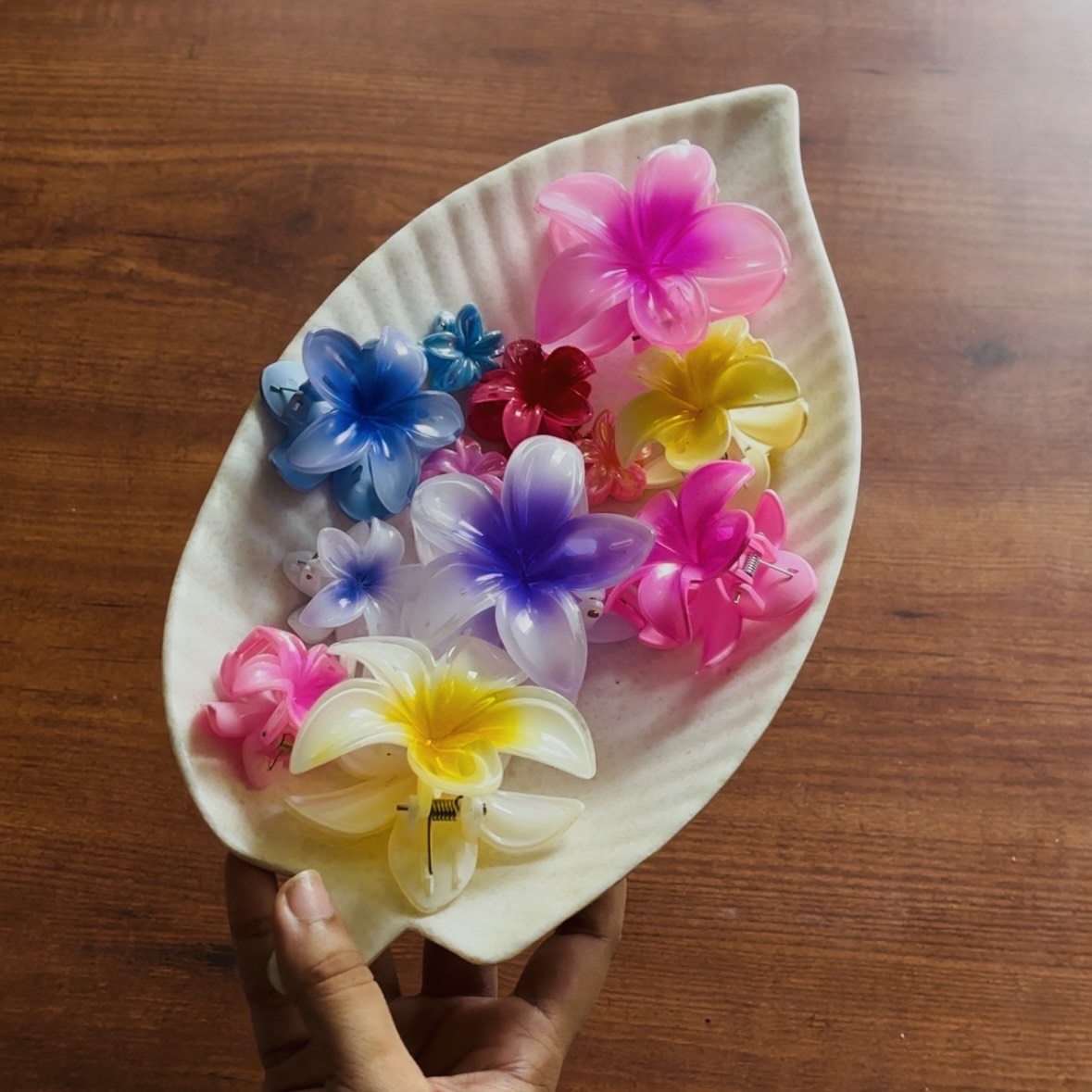 Colorful flower-shaped hair clips on a leaf-shaped holder against a wooden background. Premium Saar Beauty hair claw & chocolate bouquet with assorted flower clutchers for thick and long hair – perfect birthday gift for women and girls.
