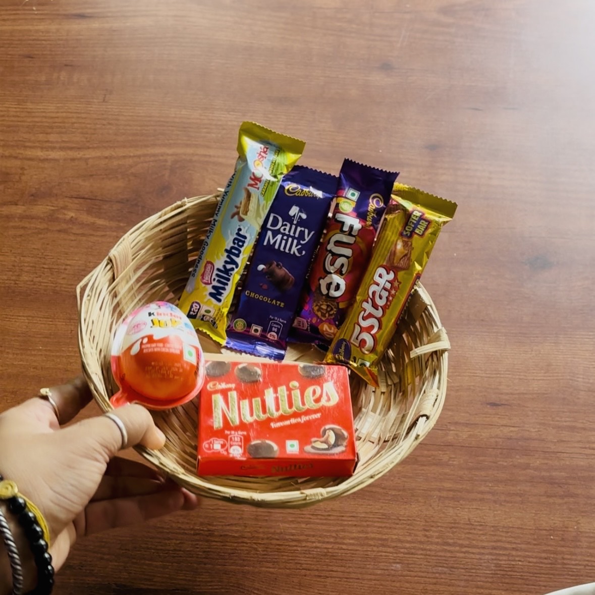 Basket of chocolate bars including Cadbury Dairy Milk and Nestle Nutties on a wooden surface.