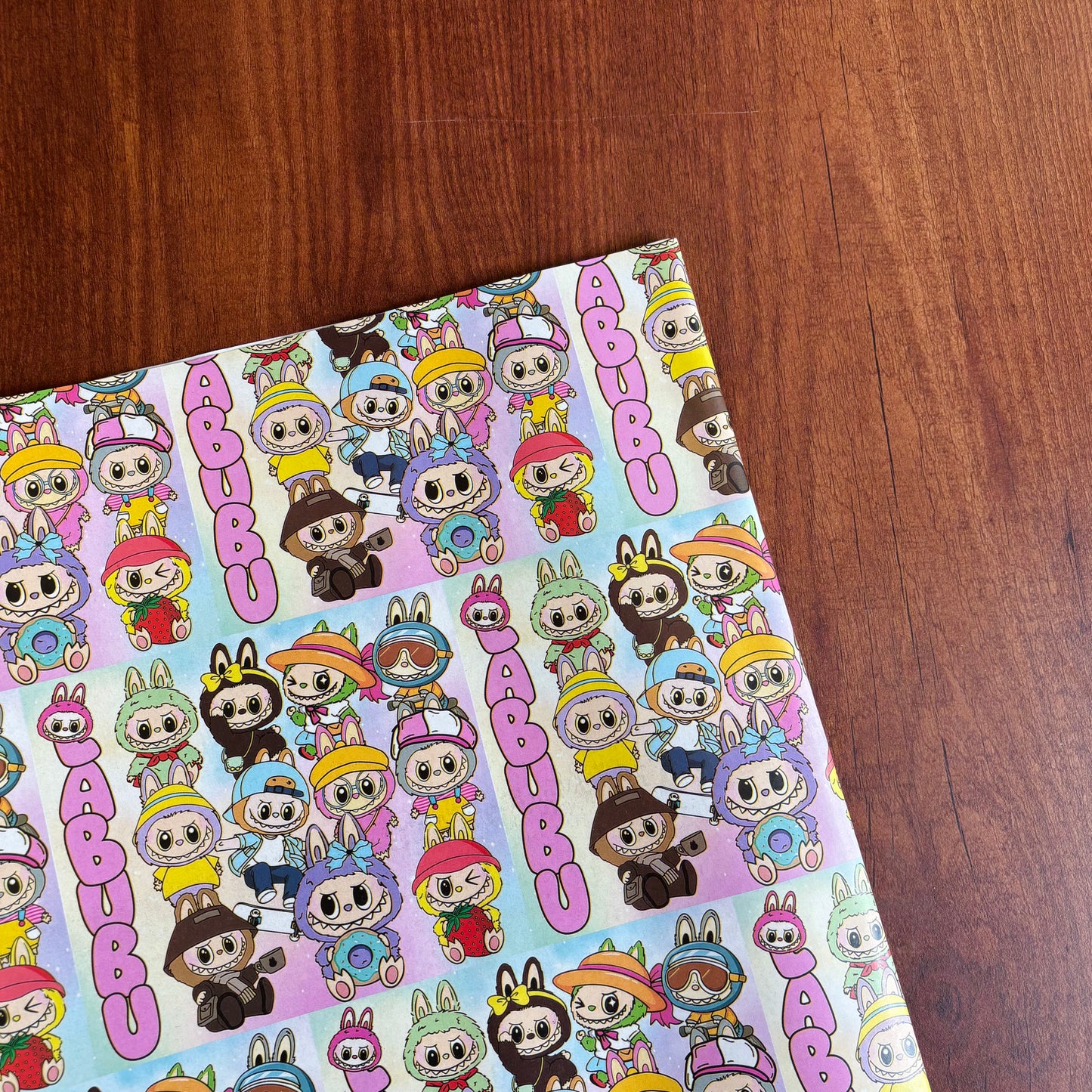 Cartoon character sheet with 'Cubcoots' branding on a wooden surface Pattern of cartoon characters with colorful hats and outfits on a light purple background. Colorful kawaii cartoon character gift wrap with playful lAbubu designs – perfect for kids and fun-loving adults