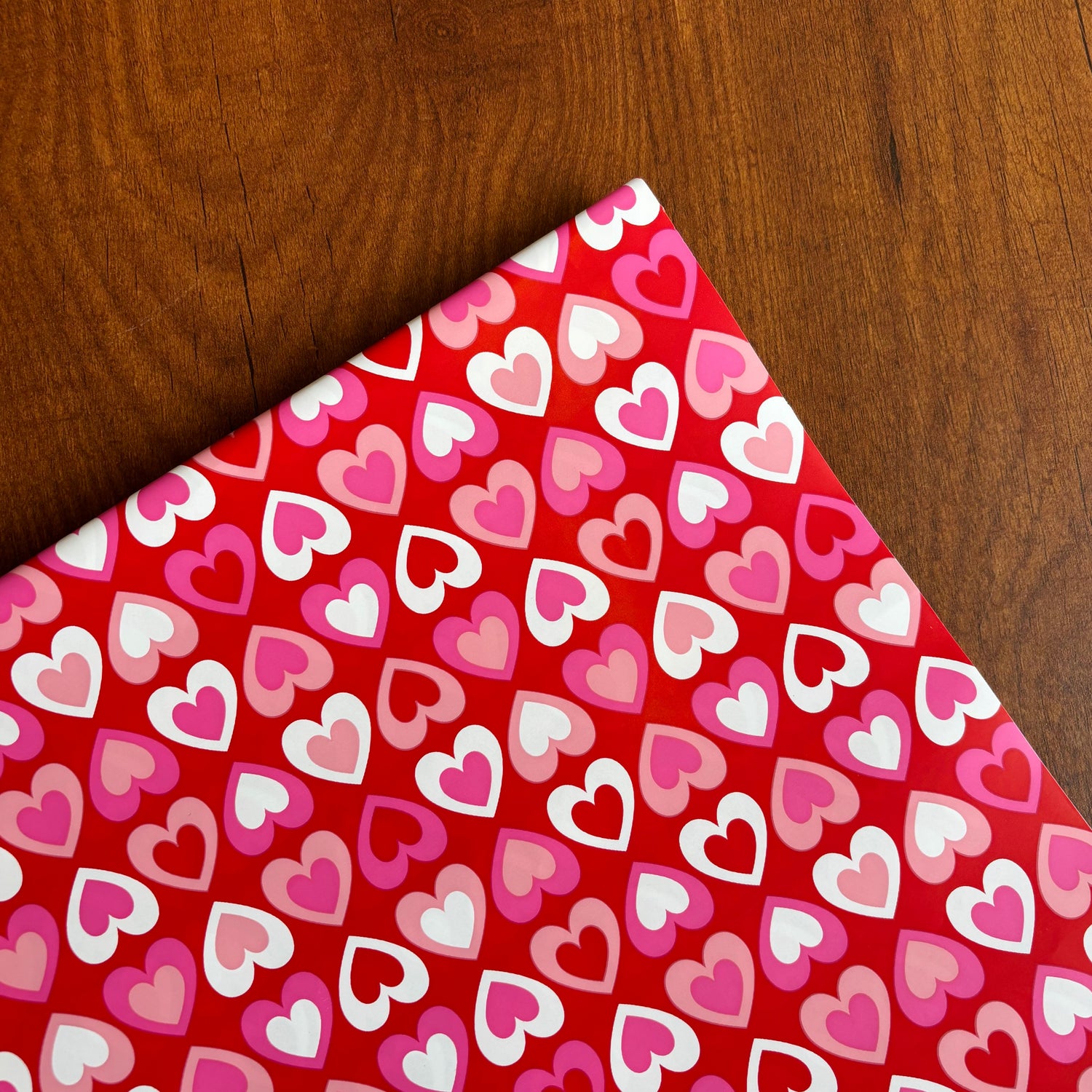Red paper with pink and white heart pattern on a wooden surface Bright red gift wrap with pink, red, and white heart pattern – perfect for Valentine’s Day and romantic gifts
