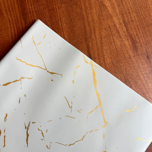 White paper with gold leaf patterns on a wooden surface Elegant white marble gift wrap with shimmering gold foil veins – perfect for luxury gifting