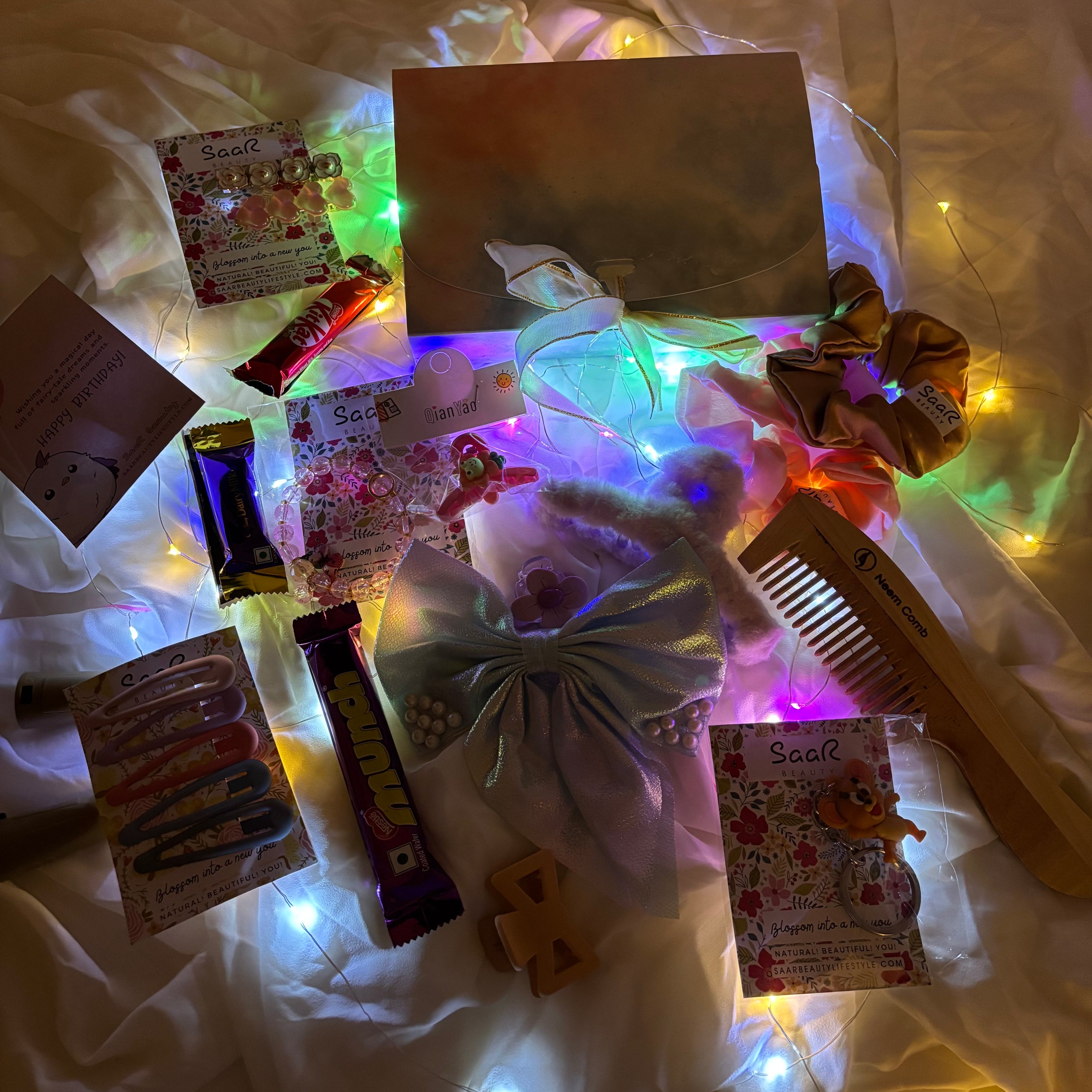 Collection of hair accessories and items on a white fabric background with string lights."Luxury birthday surprise gift box for girls with chocolates and accessories"