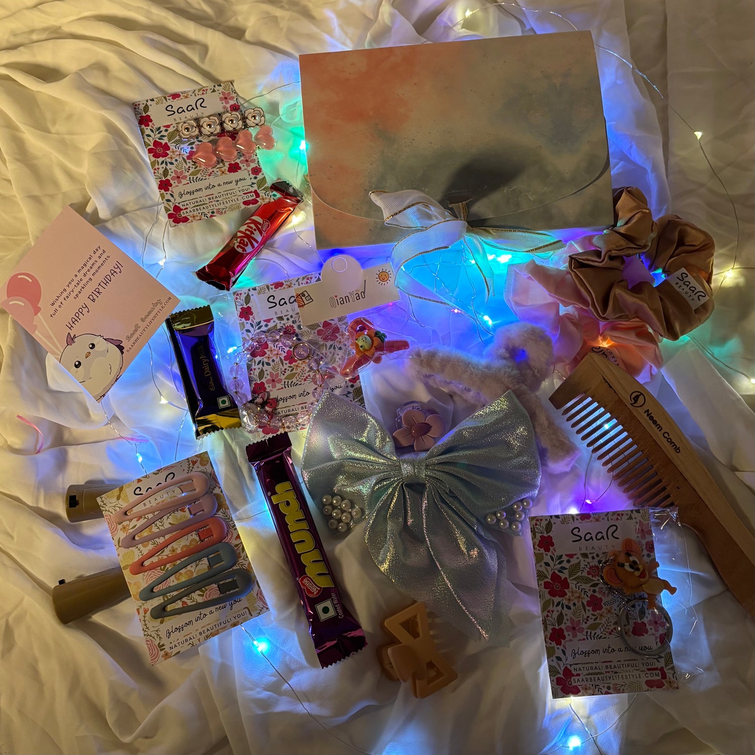 Collection of hair accessories and stationery items on a white surface with string lights."Luxury birthday surprise gift box for girls with chocolates and accessories"