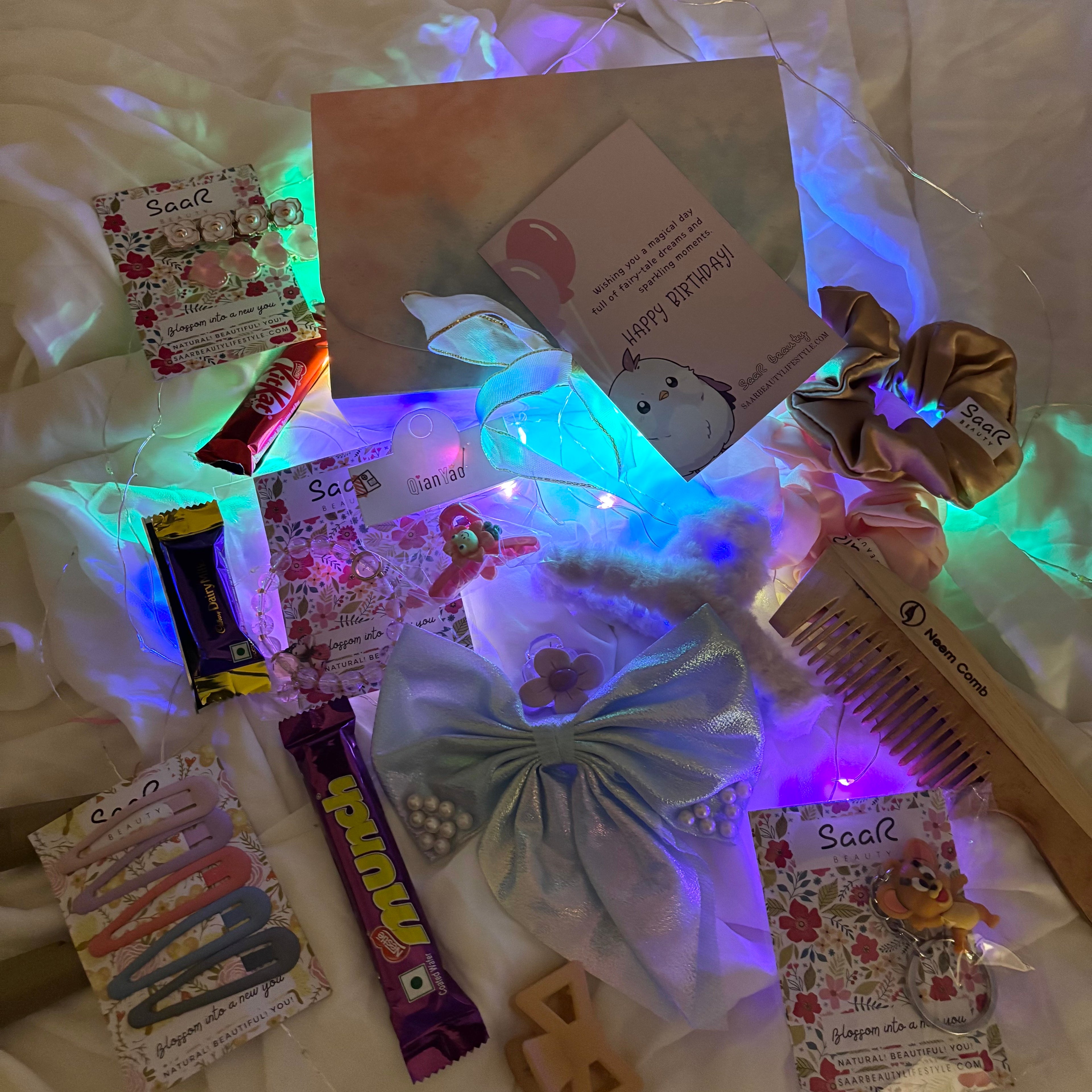 Assorted hair accessories and stationery items on a white surface with colorful lighting."Luxury birthday surprise gift box for girls with chocolates and accessories"