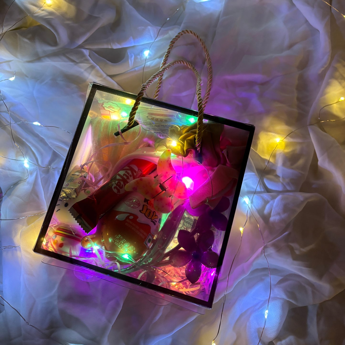 Gift hamper for women with earrings, scrunchies, clutchers and Kinder Joy Decorative gift bag with colorful lights and candy on a soft fabric background
