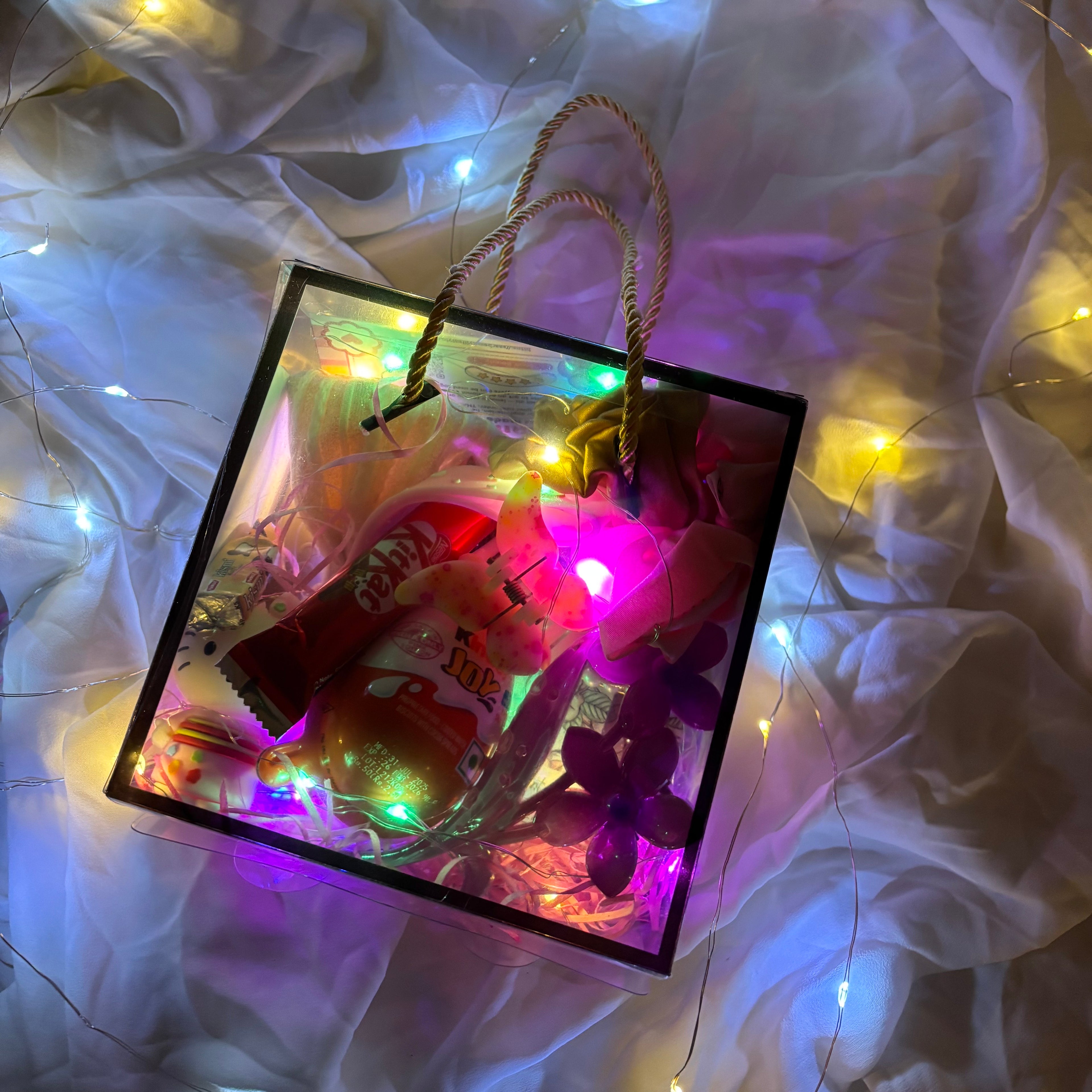 Gift hamper for women with earrings, scrunchies, clutchers and Kinder Joy Decorative gift bag with colorful lights and candy on a soft fabric background