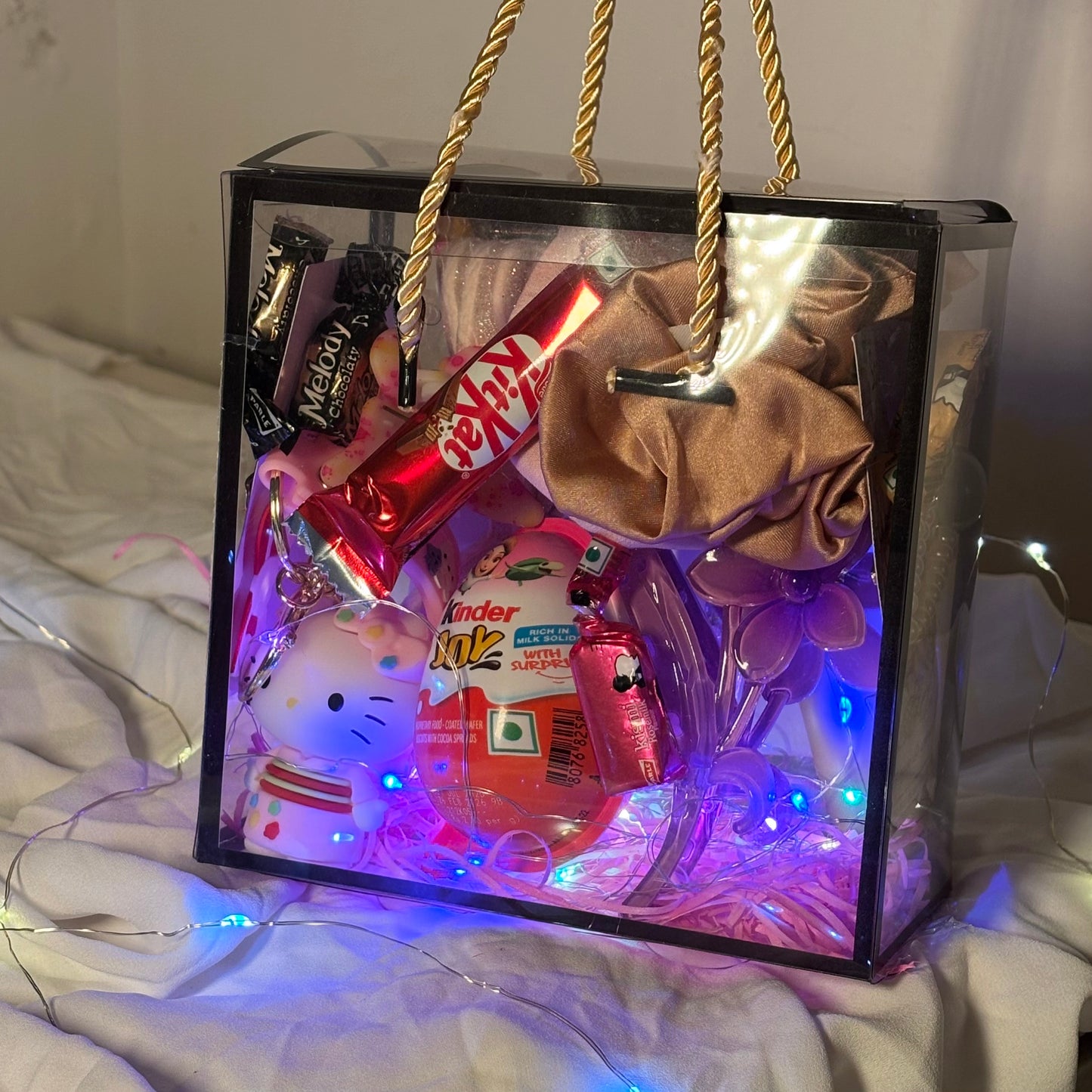 Decorative gift box with LED lights  containing small items on a white surface. Gift hamper for women with earrings, scrunchies, clutchers and Kinder Joy