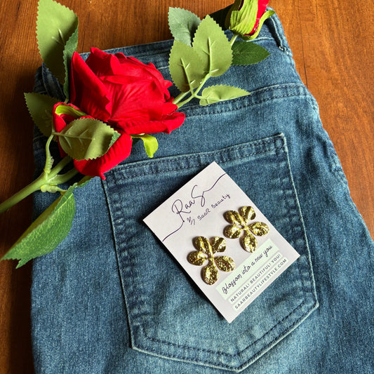 Gold floral earrings on a card in a pocket of blue jeans with a red rose and green leaves. Elegant flower stud earrings – anti-tarnish jewelry by Saar Beauty