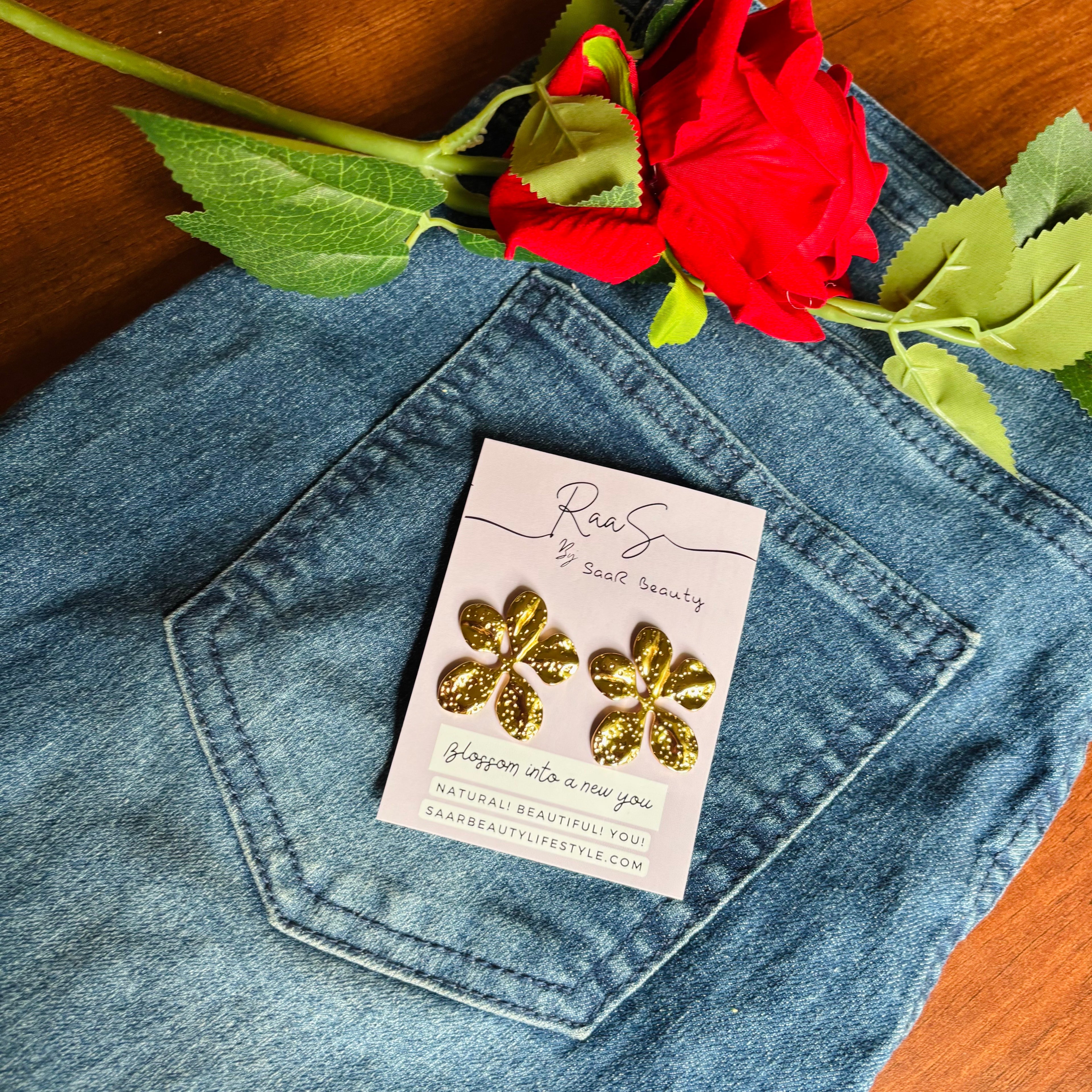 Gold flower earrings on a card in a denim pocket with a red rose.