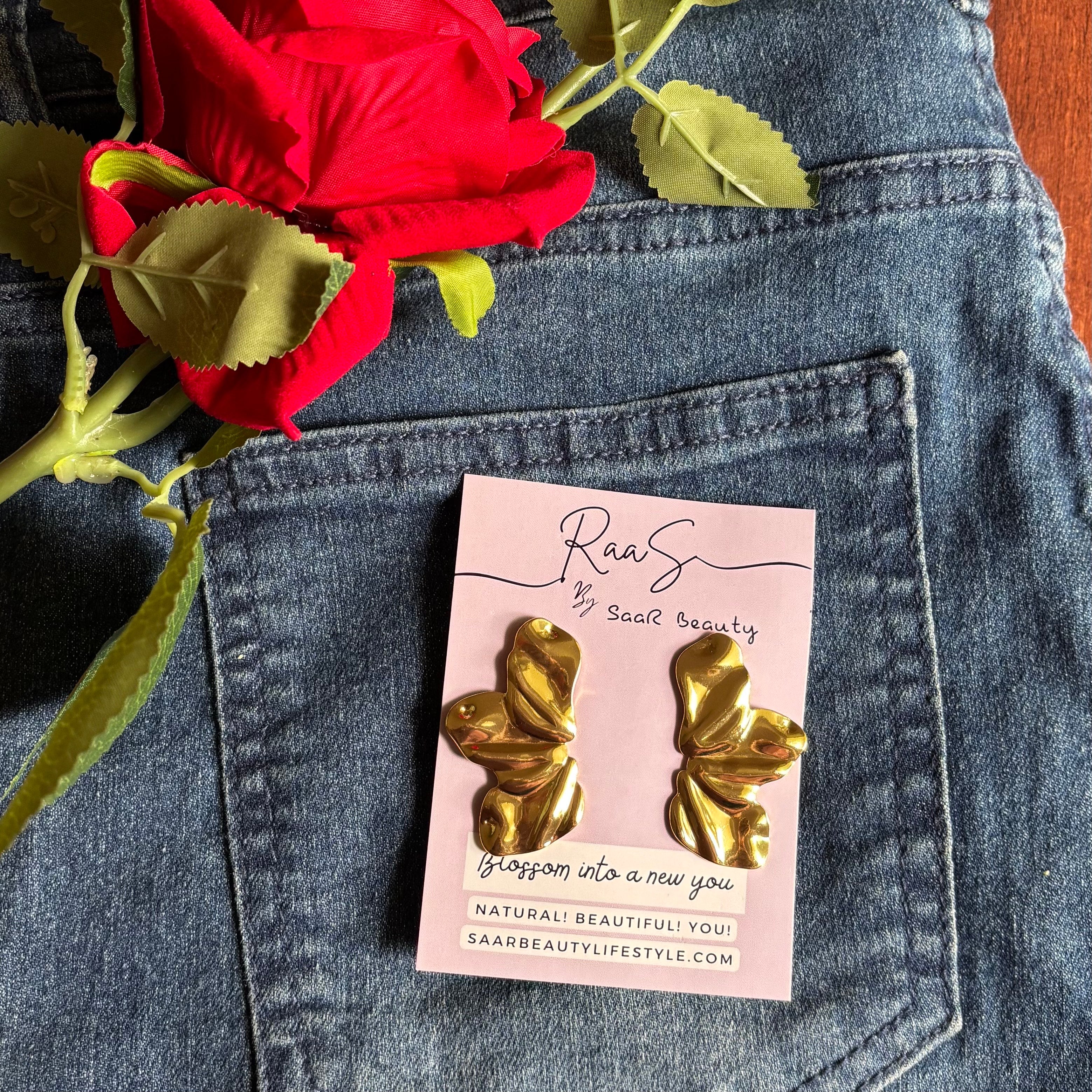 Gold earrings on a pink card with a red rose on blue denim fabric Trendy floral design gold finish earrings for women