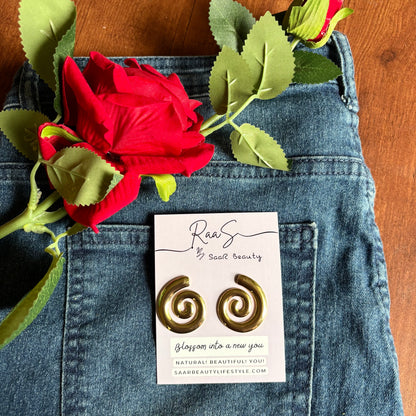 Gold spiral earrings on a card with a red rose and green leaves on blue denim fabric. 