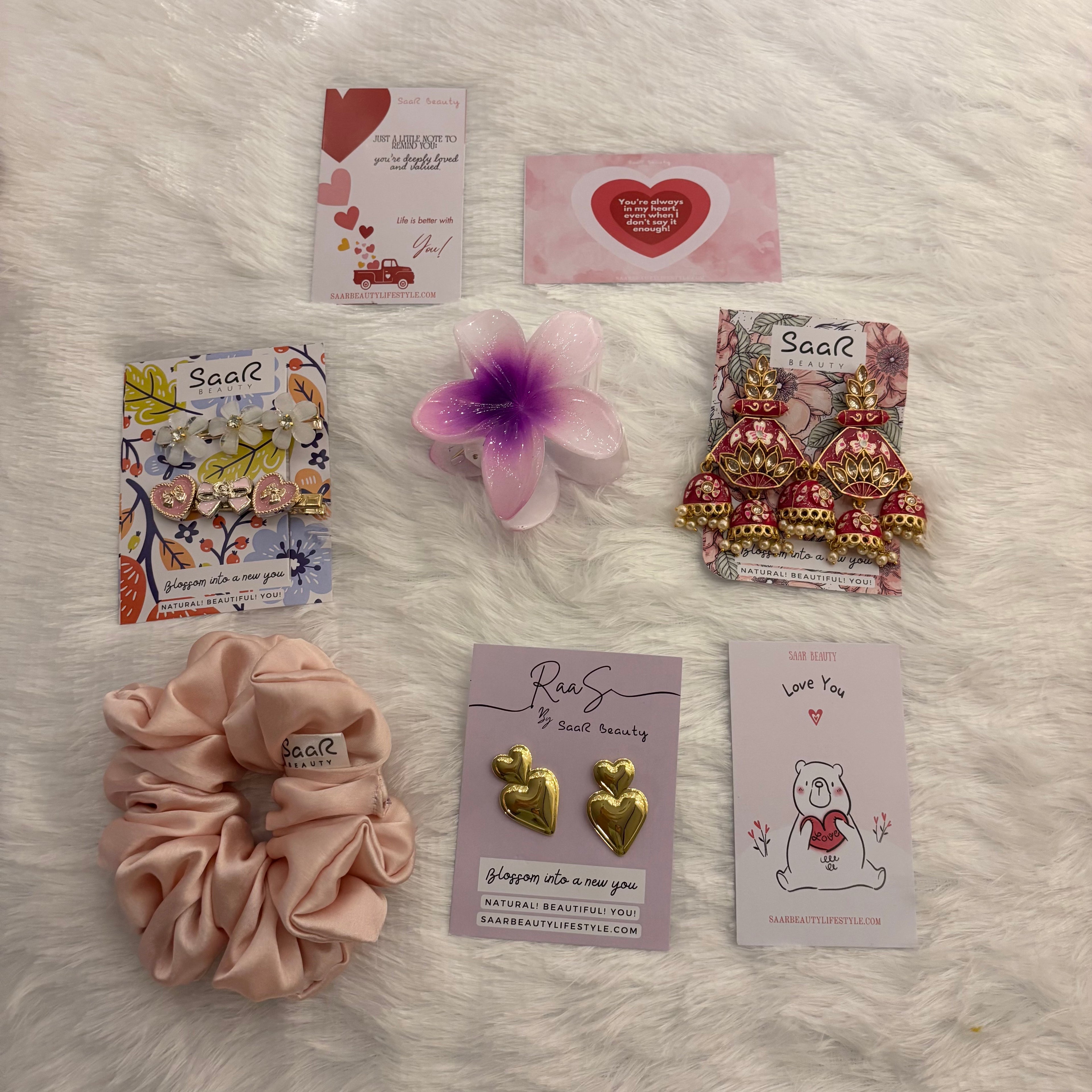 Collection of beauty products including scrunchies, earrings, and cards on a fluffy white surface. 