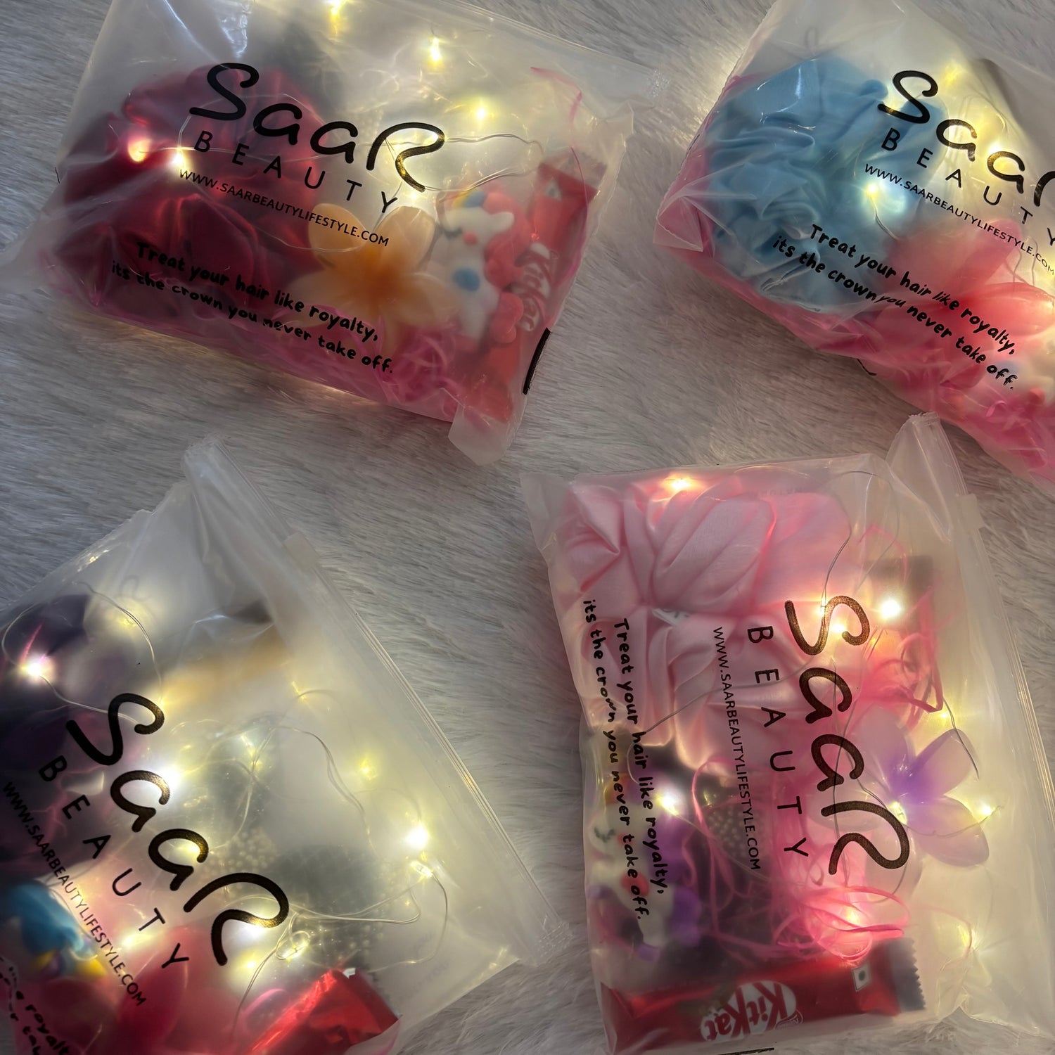 Four packages of Saar Beauty hair accessories on a white surface with string lights.Pinterest aesthetic fairy light gift hamper Saar Beauty